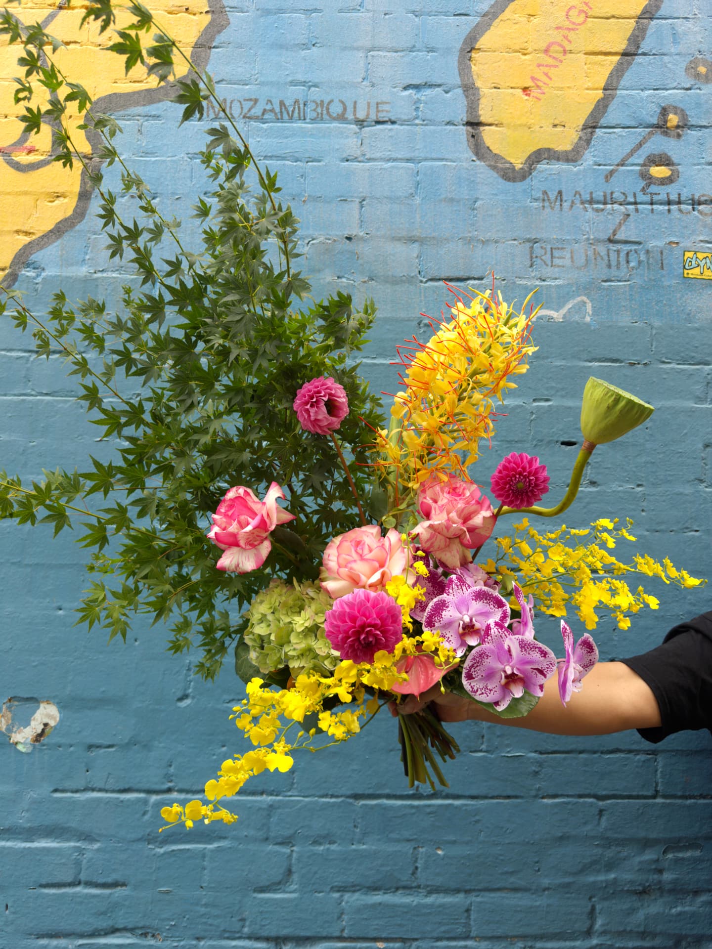 A hand-tied Flower Room bouquet held up against a Newtown mural, ready to deliver