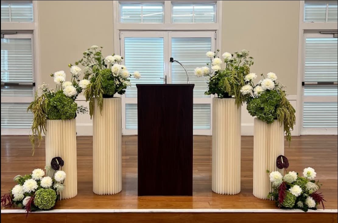 White and green flowers atop fluted plinths flanking a speaker's lectern