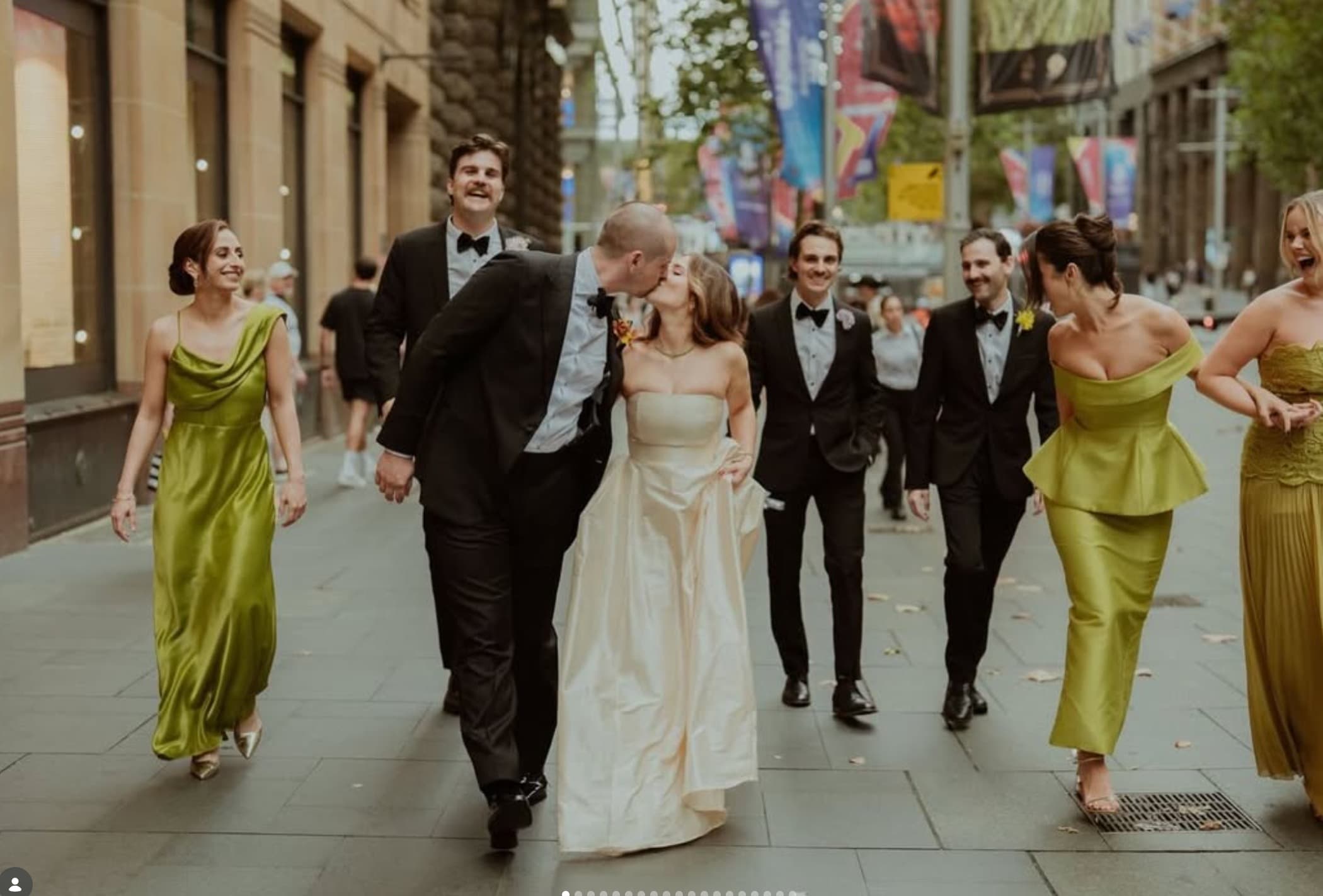 A wedding couple kissing on a Sydney street, surrounded by their party