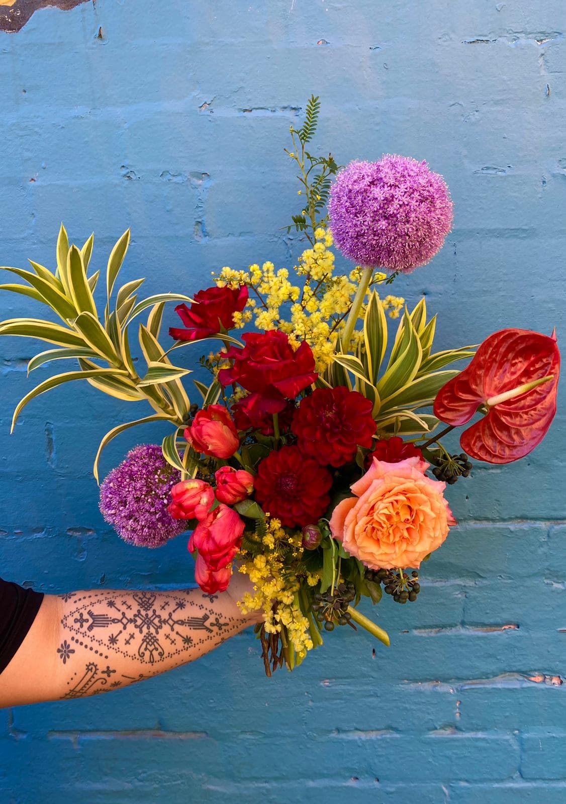 A loose hand-tied bouquet with purple allium, red anthurium and roses
