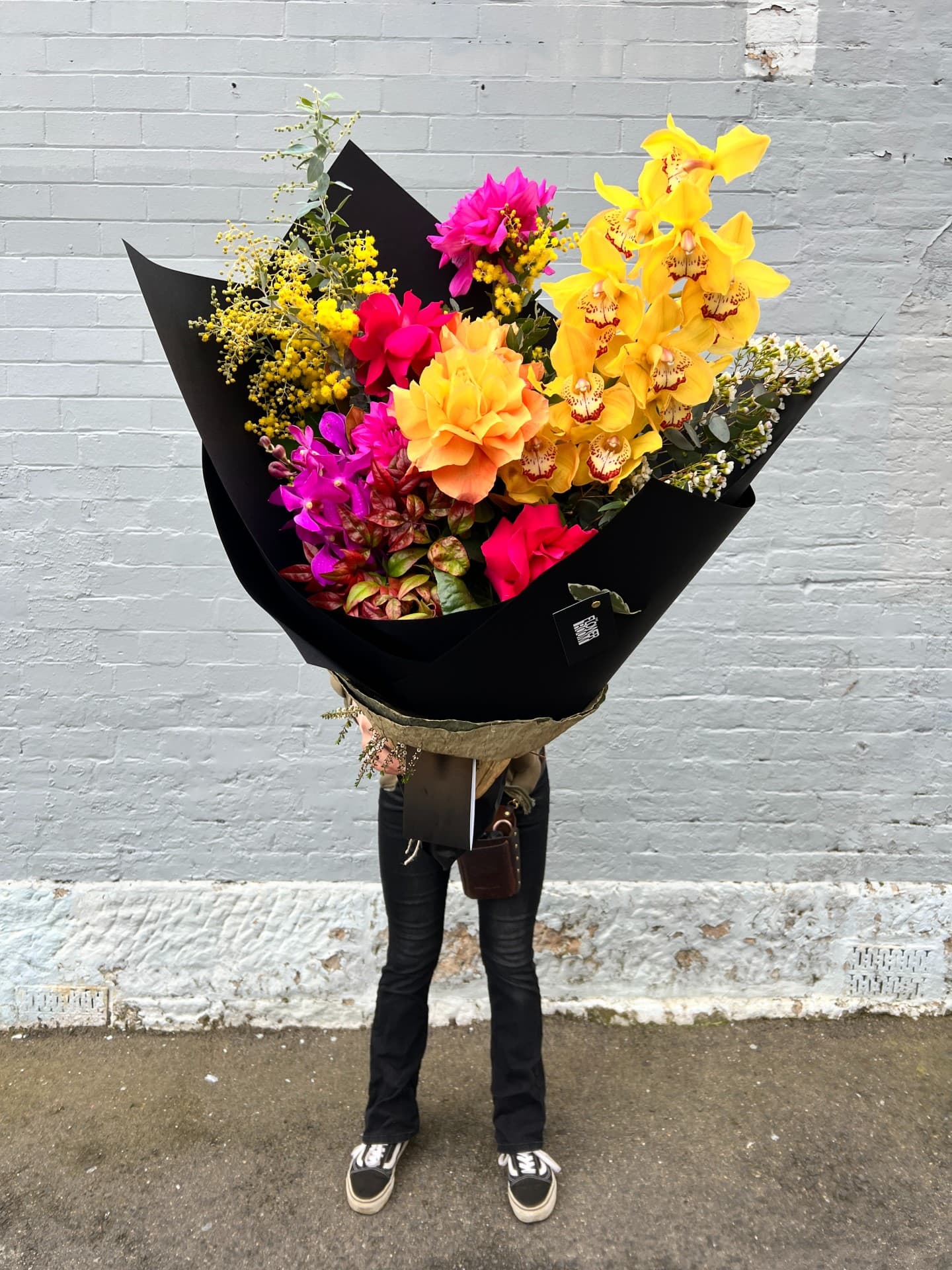 A large hand-tied bouquet of yellow orchids and pink blooms in black wrap