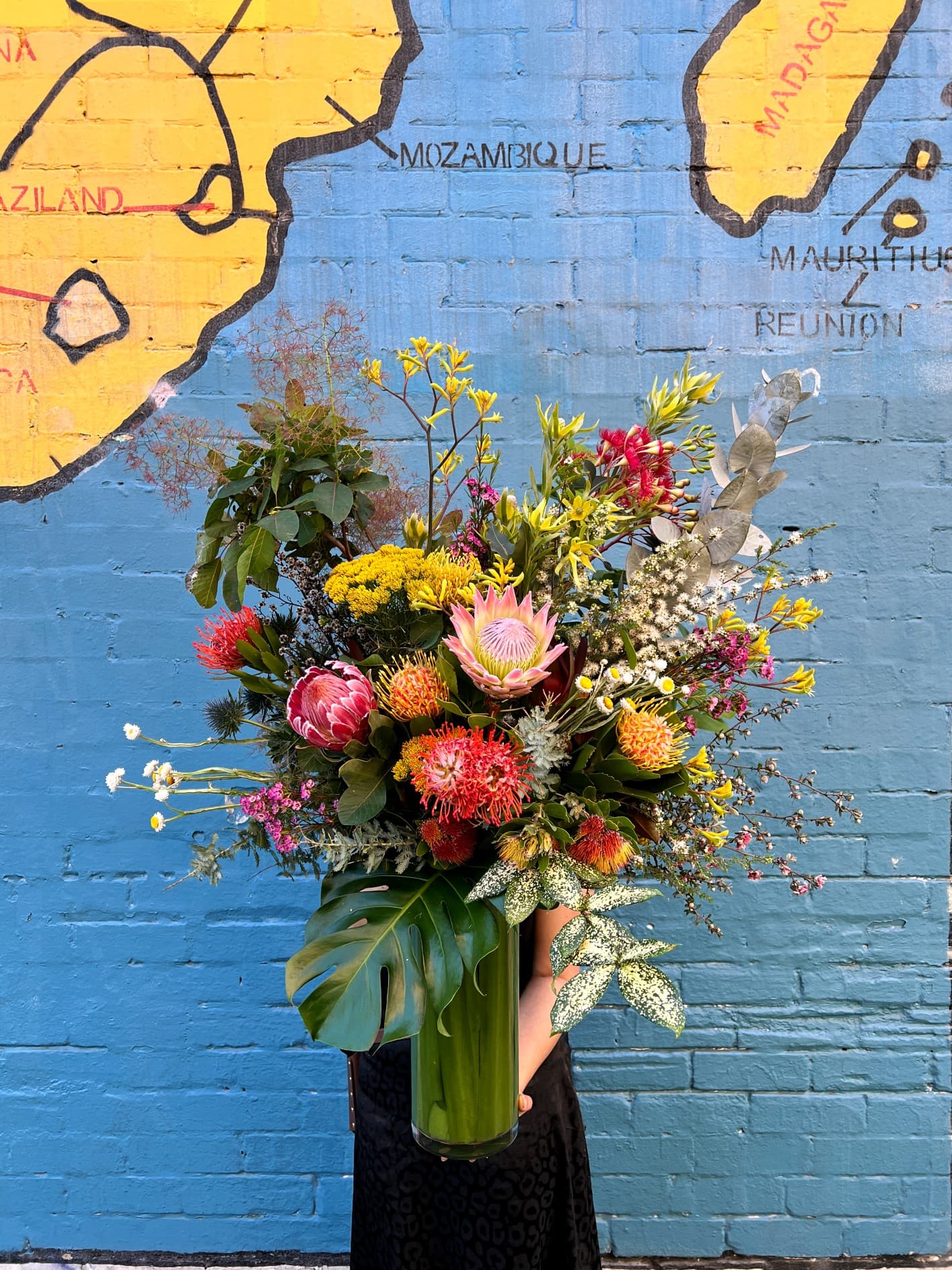 A vase of proteas, banksia and kangaroo paw against a painted mural